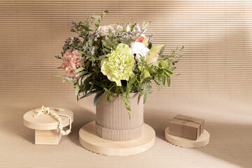 Eco friendly monochrome composition with flowers bouquet and wooden stands with DIY gift box and necklace on beige.
