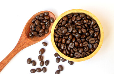 Obraz premium organic brown roasted arabica coffee beans in a wooden bowl and spoon on white background. Focus on coffee beans in a bowl. Famous and good quality coffee bean from Chiangmai, Thailand