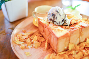French honey toast in cafe restaurant with cereals, cornflakes, vanilla ice cream, maple syrup and whipped cream on asian woman hands blurred face natural light