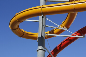 swimming pool water slide and flume in yellow and red against a cloudless blue sky

