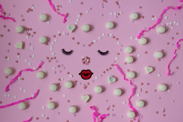 White chocolate pralines on pastel pink background. Valentine day'pattern of white candies, hearts and confetti on magenta color surface .  Birthday party  decor. Heart face with kiss and eyelashes.