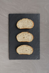 three pieces of grain bread lie on a black basalt board gray background without people close up...