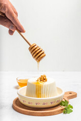 Man's hand pouring honey into a fresh cheese on a white background