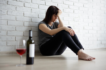 female alcoholism, relationship, divorce and depression concept - stressed woman sitting on the floor, crying and drinking wine