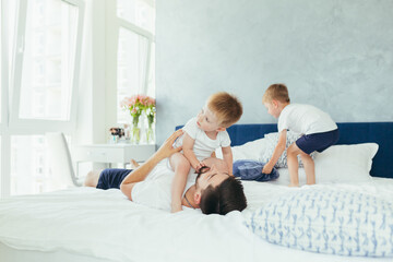 husband father playing with his children, two little boys brothers, in a large bedroom