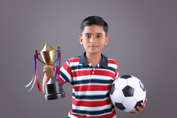 Indian school boy holding a golden trophy cup and football
