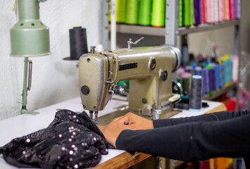 front view of an employee in a tailor's shop using a sewing machine to sew clothes. background fabric of different colors