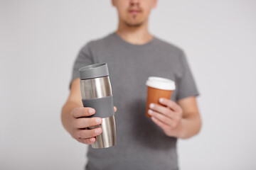 zero waste and eco friendly concept - thermo cup and disposable paper coffee cup in male hands over...