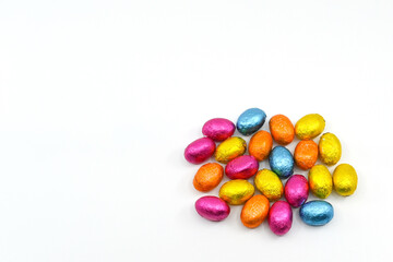 Small chocolate eggs in coloured foil wrappings on a plain background. No people.