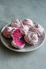 Home-made pink marshmallows lie on a plate. Gray background. Vertical photo.