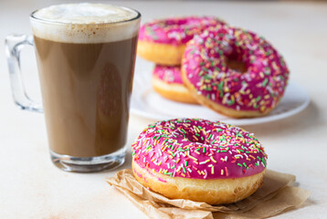 Plate sweet donuts with pink glaze and colorful sprinkles and cup of hot coffee, light concrete background.
