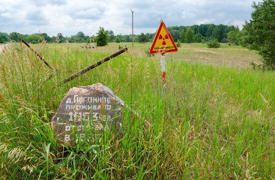 Warning sign Radioactivity and stone with commemorative inscription at entrance to resettled village of Pogonnoye in Chernobyl exclusion zone, Belarus