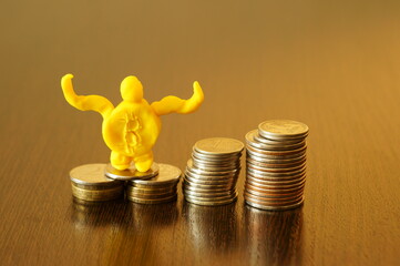 A bitcoin figurine with plasticine hands with coins on the table.