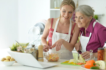 Obraz na płótnie Canvas Smiling senior mother and adult daughter cooking together at kitchen