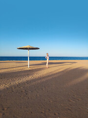 Girl on the beach with an umbrella against the blue sky, sea and yellow sand. Girl in bikini on the beach. Minimalistic photo