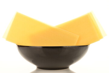 Several uncooked yellow lasagna sheets in a black ceramic plate, close-up, isolated on white.