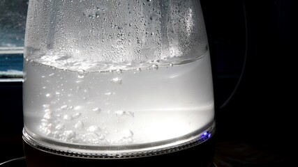 Defocused bubbles in hot water boiling inside glass teapot in bright sunlight. Closeup of boiling...