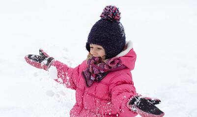 Warmly dressed little girl playing with snow close up.