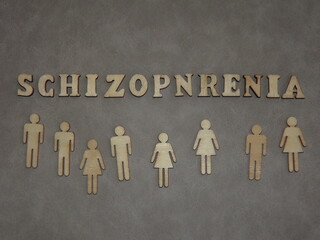 mental illness-schizophrenia in the form of wooden letters and figures of people on a gray...