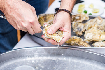 Opening an oyster with a knife on the background of a dish with oysters and lemons © Oleksii Lomako
