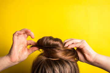 A woman makes a messy hair bun on her head. Yellow background. Copy space. Trend color of the year...