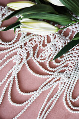 White lilies with green leaves and a necklace of pearls on a pink background.
