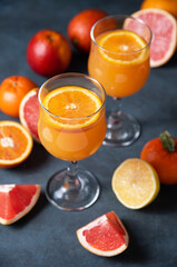 Citrus juice in two glasses and fresh fruit tangerine, orange, grapefruit and lemon on a dark gray background