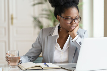 Focused young African American businesswoman or student in blazer wear glasses working at laptop at...
