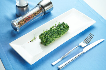 Delicious side dish for main courses - stewed spinach in cream in a white plate on a blue tablecloth
