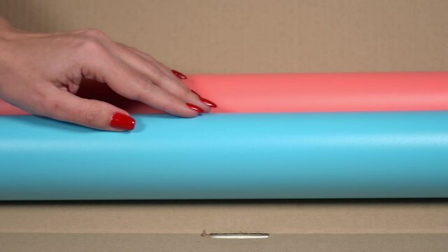 Closeup view 4k stock video footage of female hands of photographer opens brown delivery cardboard box with two new pink and blue modern pvc photo backgrounds for shooting photo sessions in studio