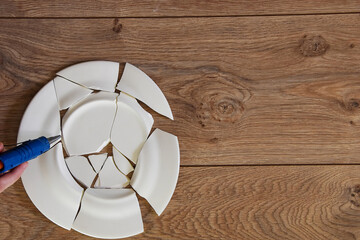 Shards of a broken plate on the wooden floor. Broken white ceramic plate on the wooden floor. Broken dishes. Top view of a damaged ceramic plate. Empty space for text.