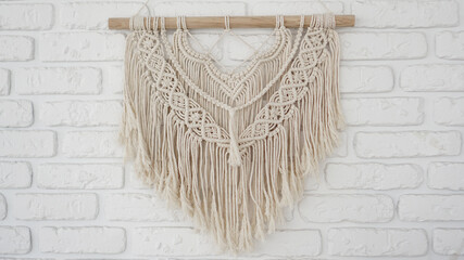 Wall panel in the style of Boho made of cotton threads in natural color on a white brick wall. Beautiful boho macrame wall panel for a cozy atmosphere © brillianata