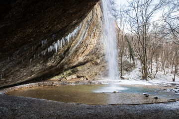 Waterfall in the winter forest. Beautiful view of the falling purest mountain river. A cliff face with icicles hanging down. Snow-covered trees, fresh air, day trips. Kozyrek waterfall in the Crimea.