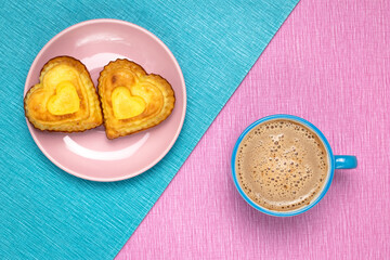 Morning coffee and heart shaped cupcakes on a pink and blue tablecloth. Romantic symbol. Valentine's day breakfast in a cafe. Ceramic cup and plate, drink and sweet food.