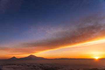 Beautiful sunset with dramatic orange clouds. The mountains in a clouds and fog. Ararat mountain.