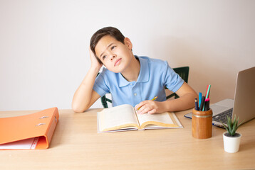 A young boy learning over his homework reading his workbook.
