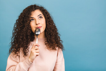 Photo of beautiful curly lady holding metal spoon in mouth look up empty space dreaming about tasty food isolated over blue background.