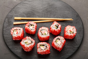 Roll with shrimp and tobiko caviar and sticks on a black round board on a gray background. Copy space