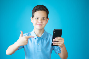 Young caucasian boy showing okay gesture with phone isolated over blue background