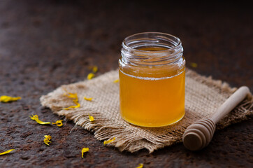 Honey in a jar with yellow daisy petals and a honey dipper. 