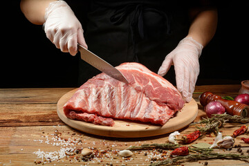 The chef uses his hands to slice pork ribs with a knife on a wooden cutting table. Selective focus. The concept of the cooking process.