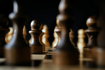Close up of black chess pieces on board. Two rows of wooden figures on chessboard on black...