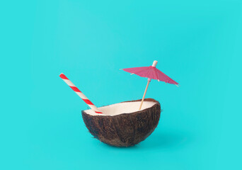 Tropical summer and vacation minimal concept. Coconut on a blue background with a cocktail straw. Vacation, travel, beach idea.