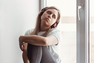 A young blonde beautiful despaired sad woman introvert with headphones is sitting on the...