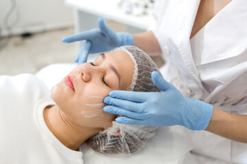 Cosmetologist massage movements apply a cleansing mask on the face of the patient close-up