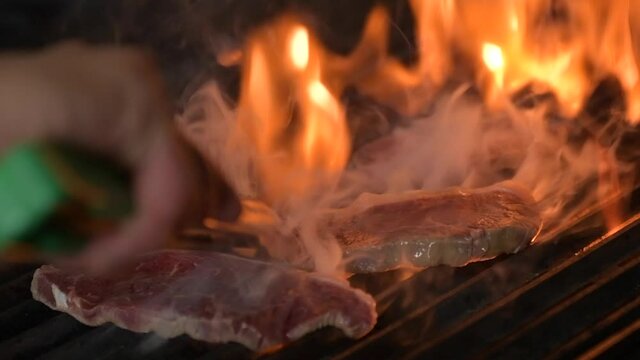 Chef turning meat on the grill. The fire is burning in slow motion. Juicy steak on the grill. BBQ Video Concept 