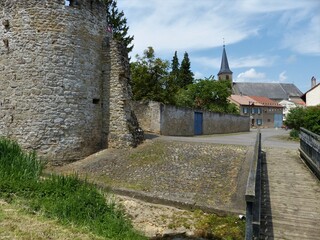 Fototapeta na wymiar Alte Stadtmauer mit Strasse und Kirche im Hintergrund in Rodemack / Frankreich