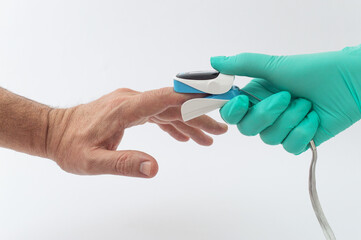 A doctor's hand in a green glove holds an oximeter to check the patient's oxygen saturation....
