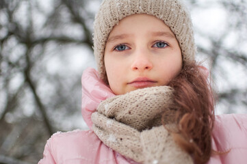 Sad child girl in warm knitted winter clothes spent time outdoors and got frozen.