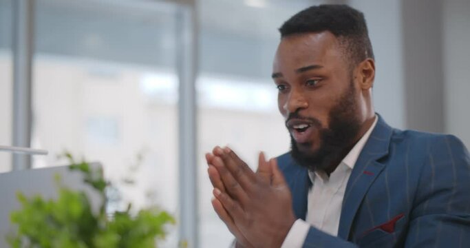 African man raising fists looking at computer screen celebrating business success in modern office